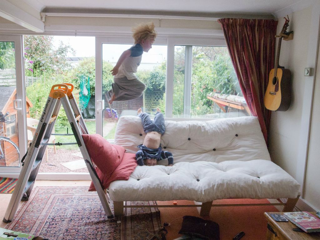 Two boys enjoy jumping on a sofa.