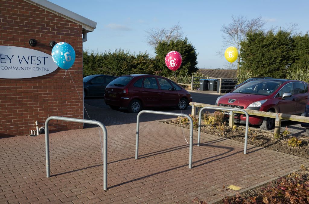 Three balloons, one blue, one red and one yellow, are tied to simple metal bike supports. The balloons all have the number six printed on them which faces the camera.