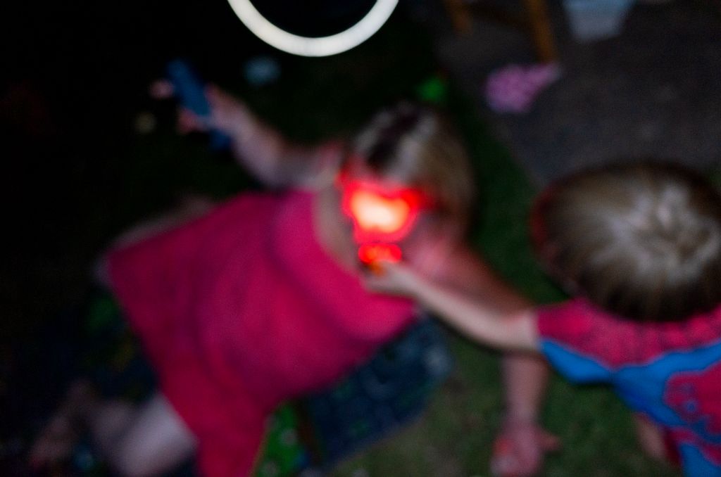 An out of focus photograph depicting a young boy shining a red light into the ladies face who appears to have fallen over.
